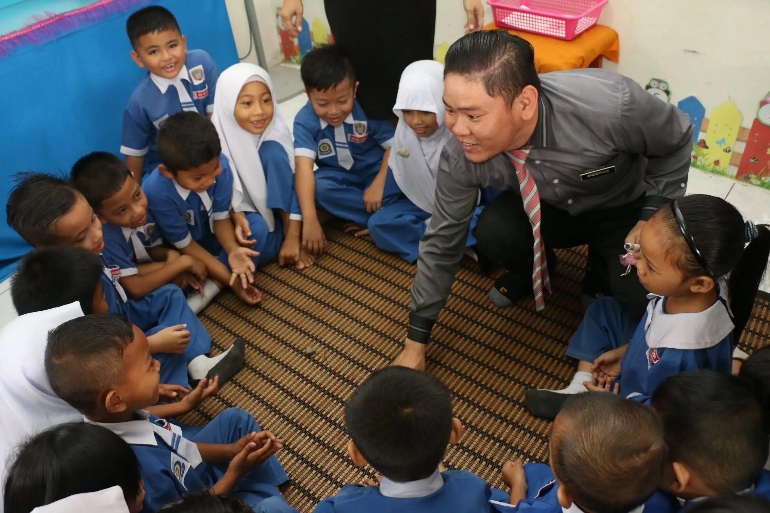 A teacher crouching to talk with young pupils seated on the classroom floor